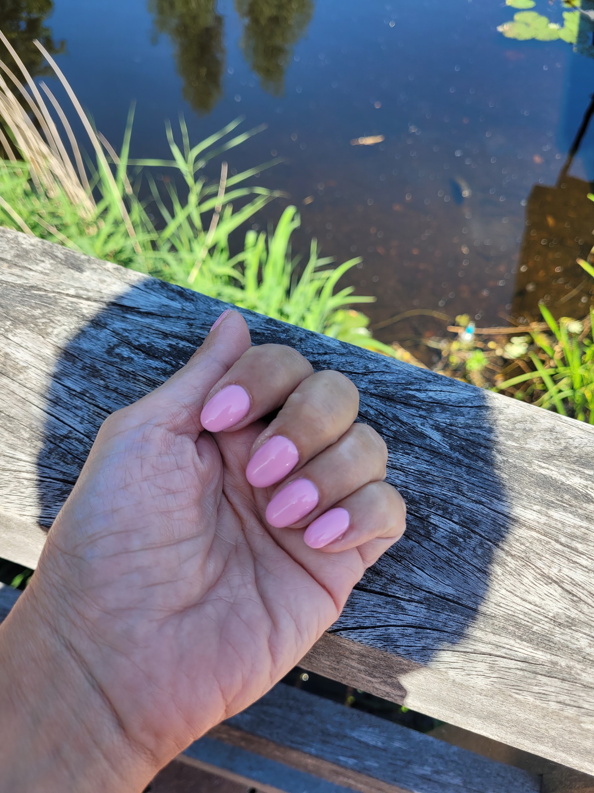 Hand met felroze BIAB-nagels op een houten reling aan het water
